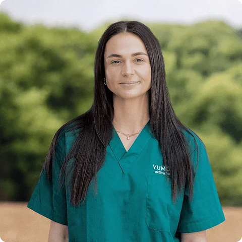 Person wearing a teal scrub top with logo against a blurred green background