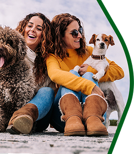 Two women sitting on the ground with two dogs, one of them holding a small dog.